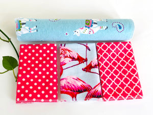 Three folded and one rolled towels with Flamingo, Lamas and Polka Dots patterns in Pink and Blue