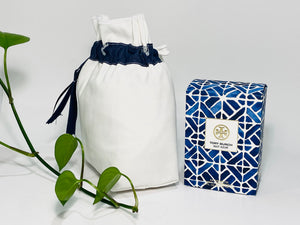 One small bag in off-white cotton canvas with a Blue Denim trim next to a bottle of perfume