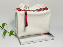 Load image into Gallery viewer, One big bag in off-white cotton canvas with a Red Paisley trim next to a book
