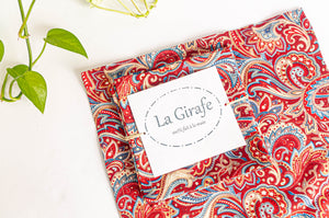 One Red Paisley napkin folded in a square on top of a flat a Red Paisley napkin