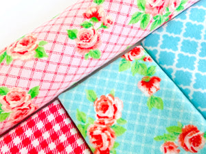 Closeup of three folded and one rolled towels with Roses and Checks patterns in Blue and Pink