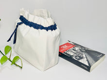 Load image into Gallery viewer, One big bag in off-white cotton canvas with a Blue Denim trim next to a book
