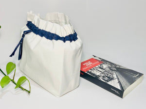 One big bag in off-white cotton canvas with a Blue Denim trim next to a book