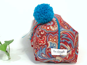 Front view of rectangular cloth cosmetic bag with zipper, Red Paisley pattern and Blue Pompon