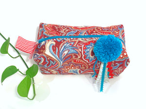 Top view of rectangular cloth cosmetic bag with zipper, Red Paisley pattern and Blue Pompon