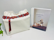Load image into Gallery viewer, One big bag in off-white cotton canvas with a Red Paisley trim next to a book
