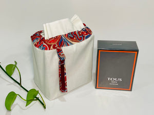 One small bag in off-white cotton canvas with a Red Paisley trim next to a bottle of perfume